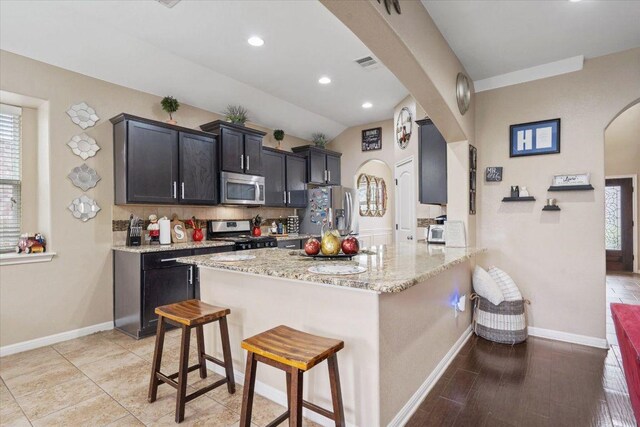 5627 Sabbia Dr, Round Rock, TX 78665 - kitchen with appliances with stainless steel finishes, arched walkways, a breakfast bar, light stone counters, and backsplash