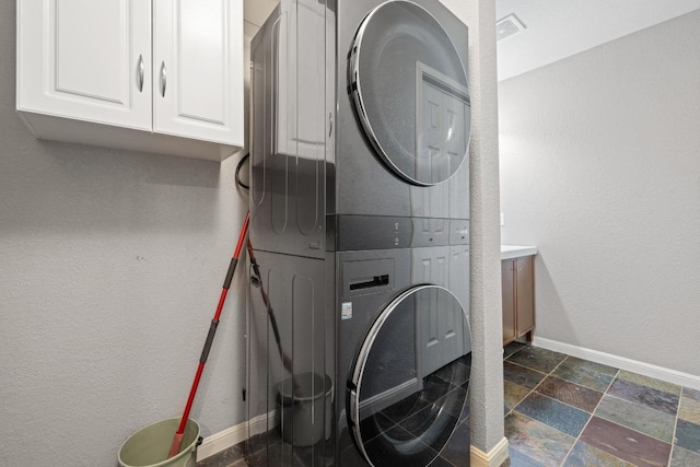 8888 Tallwood Dr Unit 1301, Austin, TX 78759 - laundry room featuring estacked washer and dryer, baseboards, cabinet space, stone tile flooring, and a textured wall