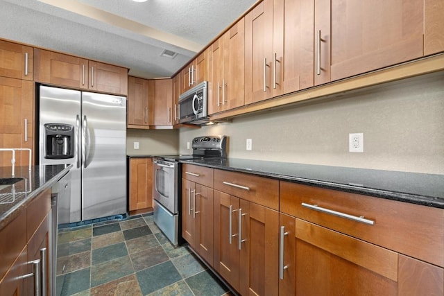 8888 Tallwood Dr Unit 1301, Austin, TX 78759 - kitchen with appliances with stainless steel finishes, brown cabinets, dark stone counters, stone finish floors, and a textured ceiling