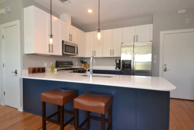 6000 S Congress Ave Unit 132, Austin, TX 78745 - kitchen with appliances with stainless steel finishes, a peninsula, a kitchen bar, light wood-style floors, and white cabinets