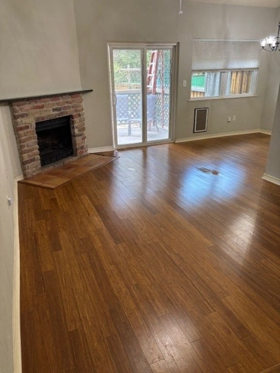 307 Quarry St, San Marcos, TX 78666 - unfurnished living room with wood finished floors, a brick fireplace, and a chandelier
