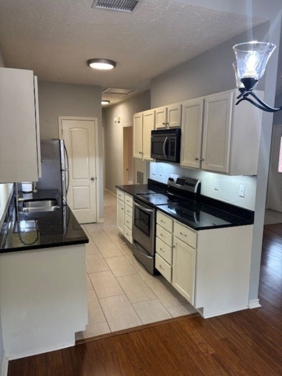 307 Quarry St, San Marcos, TX 78666 - kitchen featuring stainless steel appliances, a textured ceiling, light wood-style flooring, white cabinetry, and dark countertops