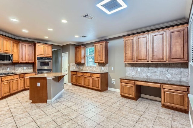2607 Deep River Cir, Round Rock, TX 78665 - kitchen with stainless steel appliances, tasteful backsplash, built in study area, ornamental molding, and brown cabinetry
