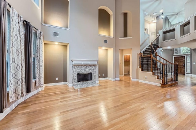 2607 Deep River Cir, Round Rock, TX 78665 - unfurnished living room featuring a tile fireplace, light wood-style floors, stairs, a high ceiling, and ceiling fan