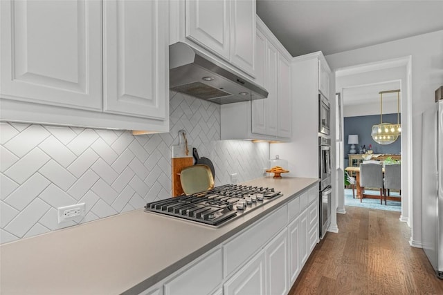 1626 Bearkat Canyon Dr, Dripping Springs, TX 78620 - kitchen with under cabinet range hood, appliances with stainless steel finishes, white cabinetry, decorative backsplash, and dark wood-type flooring