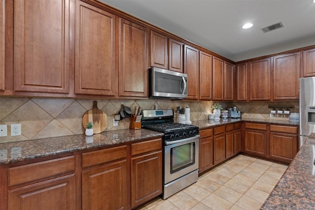 1017 Sussex Way, Round Rock, TX 78665 - kitchen featuring stainless steel appliances, brown cabinetry, tasteful backsplash, light tile patterned floors, and dark stone counters