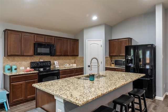 2612 American Dr, Lago Vista, TX 78645 - kitchen with black appliances, a sink, wood finished floors, tasteful backsplash, and a kitchen breakfast bar