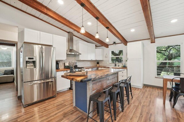360 Little Barton Dr, Dripping Springs, TX 78620 - kitchen with stainless steel fridge, wall chimney range hood, a breakfast bar, white cabinetry, and decorative backsplash