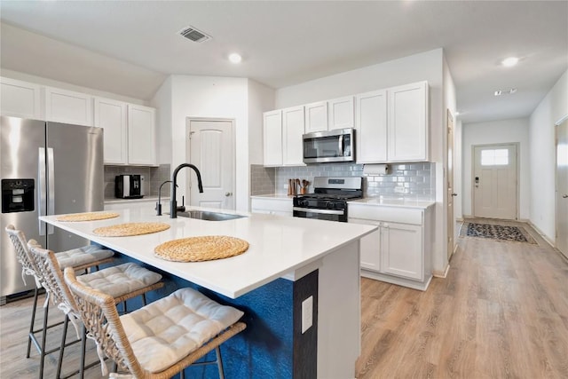 225 Sweetwater Creek Ln, Hutto, TX 78634 - kitchen featuring appliances with stainless steel finishes, a sink, light wood finished floors, a kitchen breakfast bar, and white cabinets