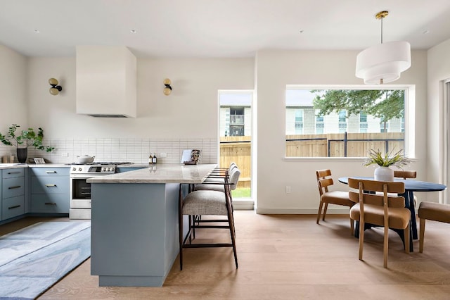 2403 E 22nd St, Austin, TX 78722 - kitchen with stainless steel gas range, gray cabinetry, a peninsula, a breakfast bar, and light wood-style floors