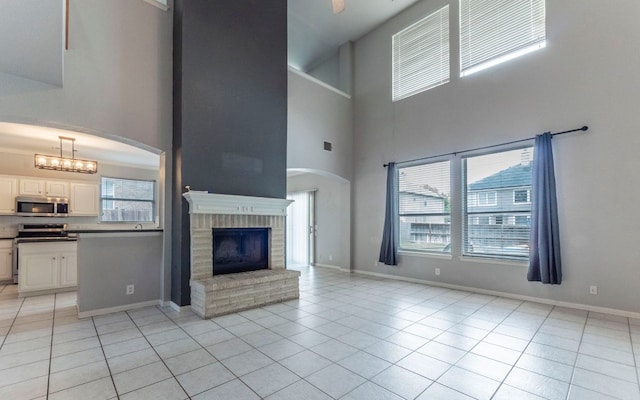 208 Settlers Valley Dr, Pflugerville, TX 78660 - unfurnished living room with a towering ceiling, healthy amount of natural light, light tile patterned floors, a fireplace, and baseboards
