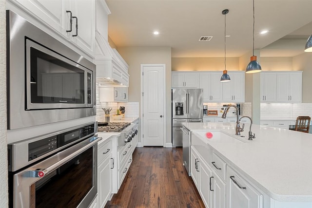 403 Baldovino Skwy, Austin, TX 78738 - kitchen featuring appliances with stainless steel finishes, white cabinetry, dark wood-type flooring, decorative backsplash, and an island with sink