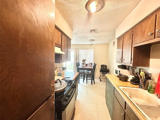 5005 S Pleasant Valley Rd, Austin, TX 78744 - kitchen with gas range, freestanding refrigerator, a textured ceiling, under cabinet range hood, and light countertops