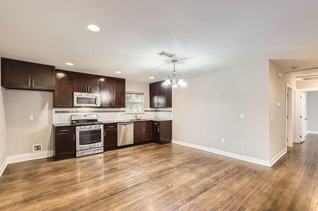 704 Wren Ave, Austin, TX 78753 - kitchen featuring stainless steel appliances, dark brown cabinetry, tasteful backsplash, hardwood / wood-style flooring, and a chandelier
