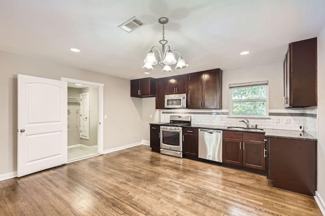 704 Wren Ave, Austin, TX 78753 - kitchen featuring appliances with stainless steel finishes, a chandelier, light wood finished floors, dark countertops, and dark brown cabinets