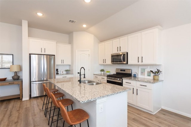 2208 Mcclendon Trl, Leander, TX 78641 - kitchen with stainless steel appliances, a sink, a breakfast bar area, white cabinetry, and a kitchen island with sink