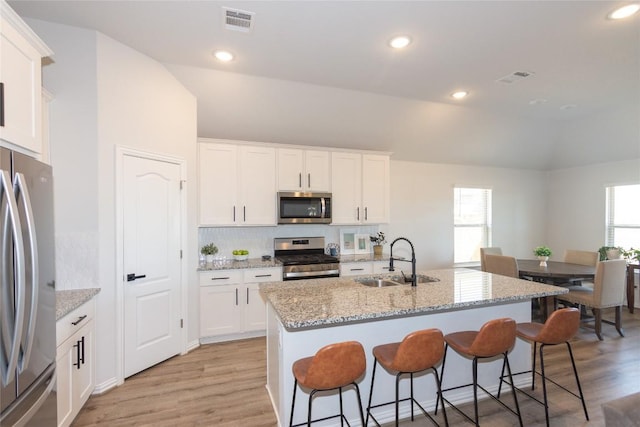 2208 Mcclendon Trl, Leander, TX 78641 - kitchen featuring stainless steel appliances, a sink, vaulted ceiling, light wood finished floors, and a breakfast bar