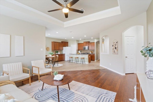 3408 Glastonbury Trl, Pflugerville, TX 78660 - living area with light wood-style floors, a raised ceiling, arched walkways, a ceiling fan, and baseboards