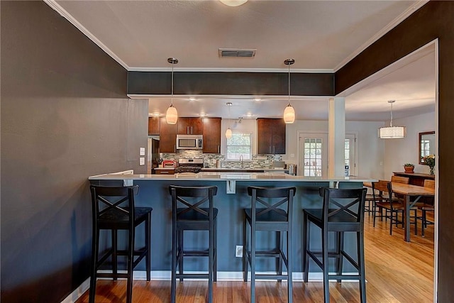 1706 Ridgemont Dr, Austin, TX 78723 - kitchen featuring appliances with stainless steel finishes, wood finished floors, light countertops, a breakfast bar, and decorative backsplash