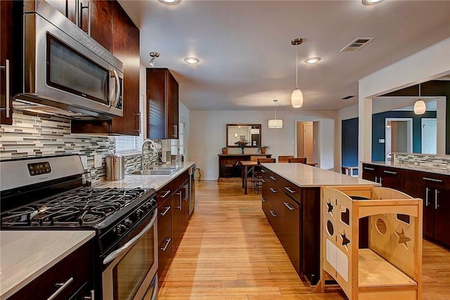 1706 Ridgemont Dr, Austin, TX 78723 - kitchen featuring appliances with stainless steel finishes, a sink, a center island, light wood finished floors, and light countertops