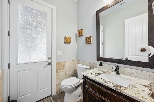 7617 Lazy River Cv, Austin, TX 78730 - half bathroom featuring vanity, toilet, tile walls, and a wainscoted wall