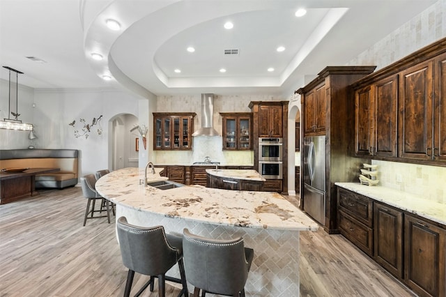 7617 Lazy River Cv, Austin, TX 78730 - kitchen featuring arched walkways, wall chimney range hood, an island with sink, stainless steel appliances, and a sink