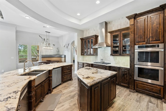 7617 Lazy River Cv, Austin, TX 78730 - kitchen with wall chimney exhaust hood, stainless steel appliances, light wood finished floors, decorative backsplash, and dark brown cabinetry