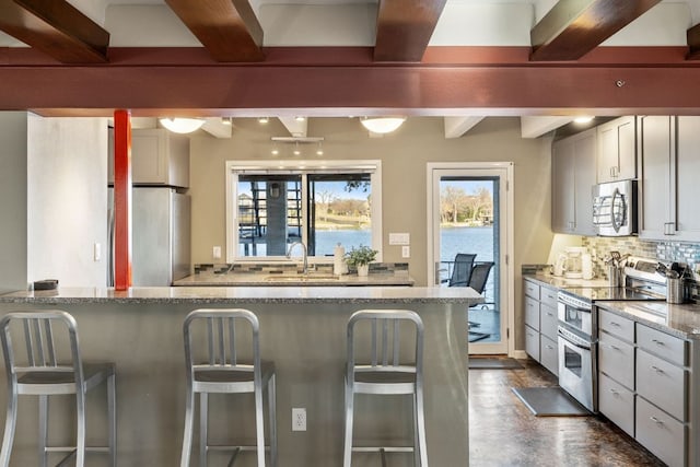 421 Yucca Dr, Kingsland, TX 78639 - kitchen featuring stainless steel appliances, beam ceiling, a kitchen breakfast bar, backsplash, and light stone counters