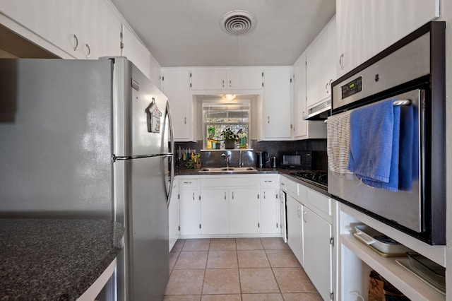 4701 Sylvandale Dr Unit 1, Austin, TX 78745 - kitchen with stainless steel appliances, light tile patterned floors, backsplash, white cabinets, and under cabinet range hood