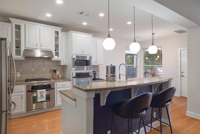 6305 Carrington Dr, Austin, TX 78749 - kitchen with stainless steel appliances, under cabinet range hood, backsplash, white cabinets, and light wood finished floors