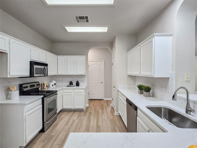 9403 Tea Rose Trl, Austin, TX 78748 - kitchen featuring stainless steel appliances, a sink, arched walkways, light wood-type flooring, and white cabinetry