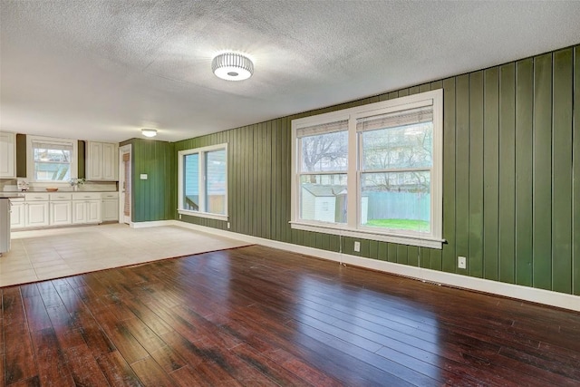 1309 E 13th St, Austin, TX 78702 - unfurnished living room with light wood finished floors, a textured ceiling, baseboards, and wooden walls