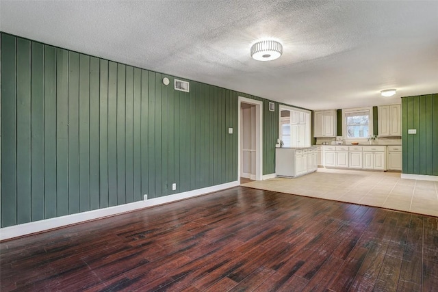 1309 E 13th St, Austin, TX 78702 - unfurnished living room with light wood finished floors, baseboards, wooden walls, and a textured ceiling