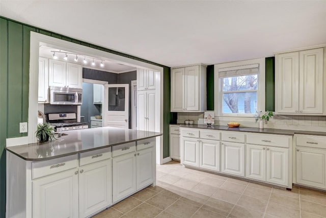 1309 E 13th St, Austin, TX 78702 - kitchen with appliances with stainless steel finishes, dark countertops, light tile patterned flooring, and white cabinets