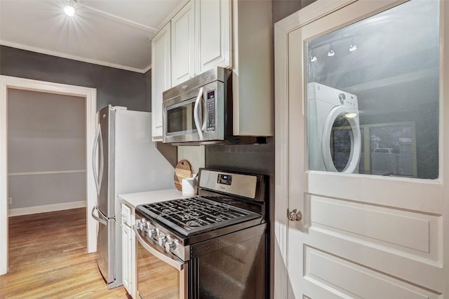 1309 E 13th St, Austin, TX 78702 - kitchen featuring appliances with stainless steel finishes, washer / clothes dryer, light wood-type flooring, white cabinetry, and baseboards