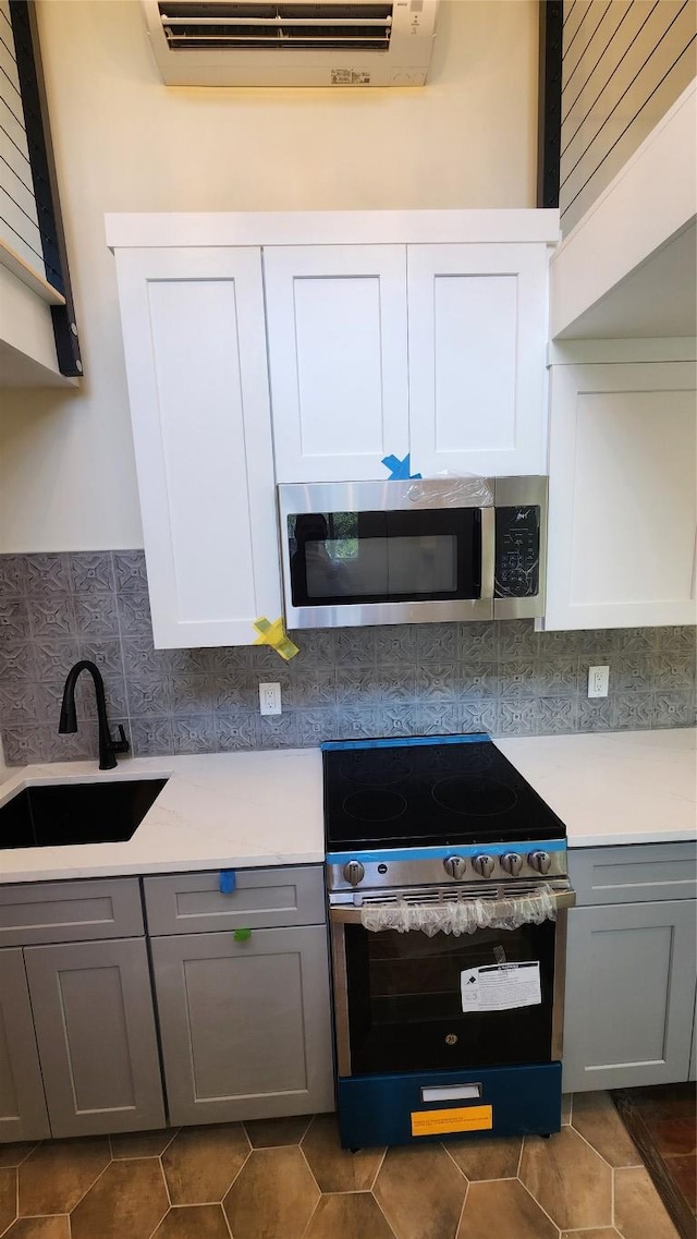 1134 Lott Ave, Austin, TX 78721 - kitchen with stainless steel appliances, a sink, gray cabinetry, backsplash, and light countertops