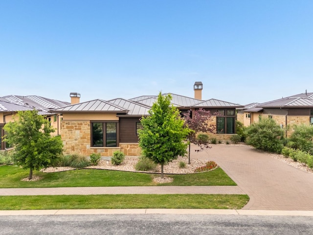 2317 Kahala Sunset Dr, Spicewood, TX 78669 - view of front facade featuring a standing seam roof, a chimney, a metal roof, decorative driveway, and stone siding