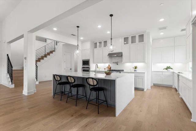 3008 Soldato Way, Leander, TX 78641 - kitchen featuring under cabinet range hood, appliances with stainless steel finishes, tasteful backsplash, light wood-style flooring, and a kitchen island with sink