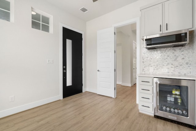 504 Tomichi Trl, Austin, TX 78738 - kitchen featuring wine cooler, stainless steel microwave, decorative backsplash, light wood finished floors, and baseboards