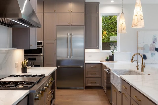 4600 Parkdale Pl Unit 1, Austin, TX 78745 - kitchen featuring stainless steel appliances, wall chimney range hood, light wood-style flooring, gray cabinetry, and light stone counters