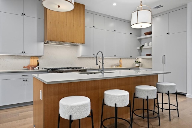 2635 Barton Hills Dr, Austin, TX 78704 - kitchen featuring open shelves, decorative backsplash, light countertops, decorative light fixtures, and a center island with sink