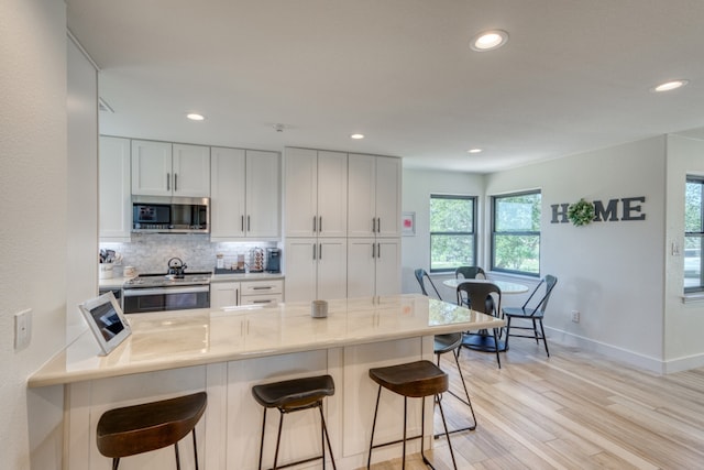 3305 Close Call, Horseshoe Bay, TX 78657 - kitchen featuring stainless steel appliances, baseboards, light wood-style floors, tasteful backsplash, and a breakfast bar
