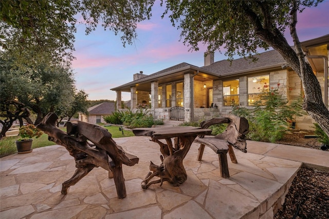 201 Greenridge Ln, Dripping Springs, TX 78620 - back of property at dusk featuring stone siding, a chimney, and a patio area