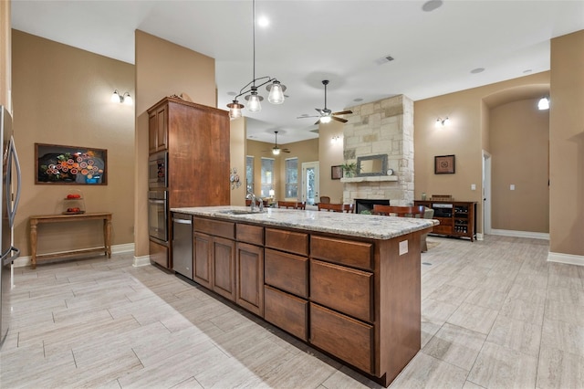 201 Greenridge Ln, Dripping Springs, TX 78620 - kitchen with appliances with stainless steel finishes, a ceiling fan, a fireplace, brown cabinetry, and a peninsula