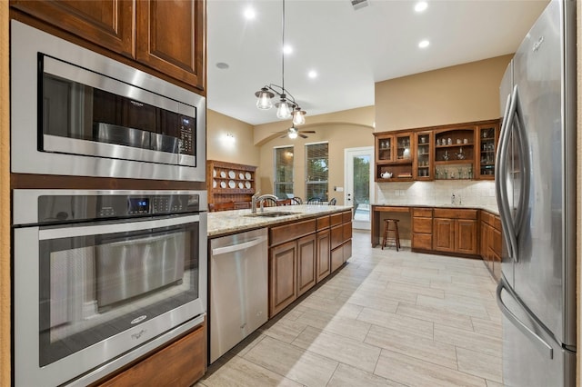 201 Greenridge Ln, Dripping Springs, TX 78620 - kitchen with appliances with stainless steel finishes, brown cabinets, tasteful backsplash, light stone countertops, and ceiling fan