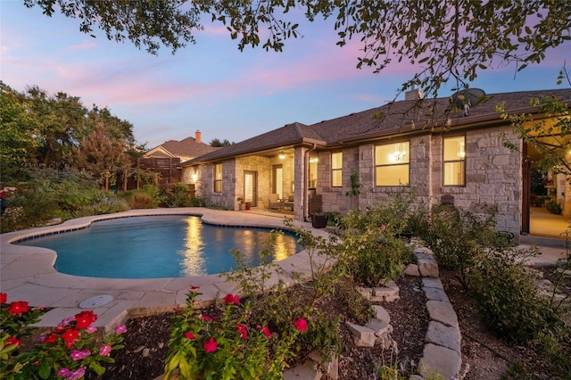 201 Greenridge Ln, Dripping Springs, TX 78620 - back of house at dusk featuring stone siding, a patio, a chimney, and an outdoor pool