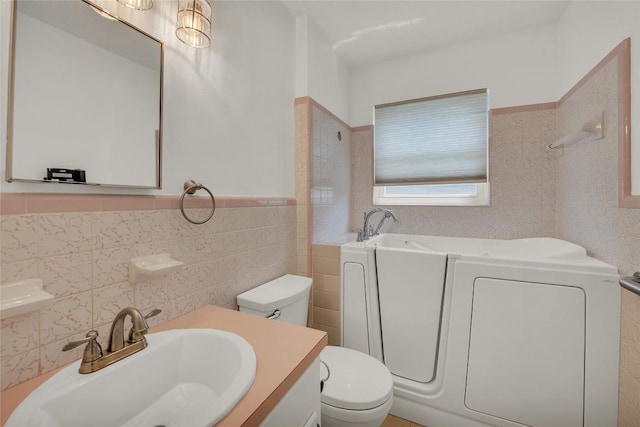 1009 Robertson Ave, Copperas Cove, TX 76522 - bathroom featuring tile walls, toilet, a bath, vanity, and a wainscoted wall