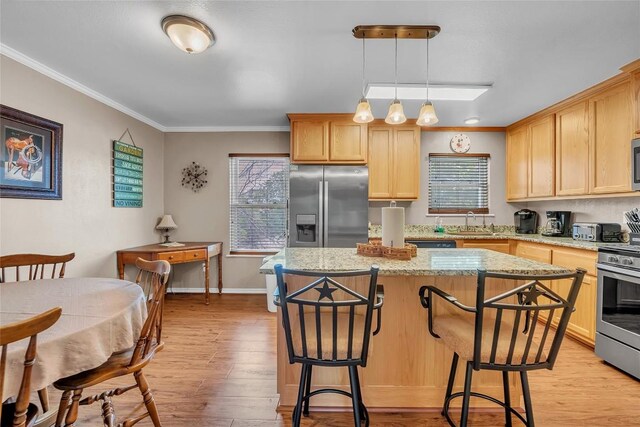 1009 Robertson Ave, Copperas Cove, TX 76522 - kitchen with appliances with stainless steel finishes, ornamental molding, a kitchen bar, light wood finished floors, and a center island