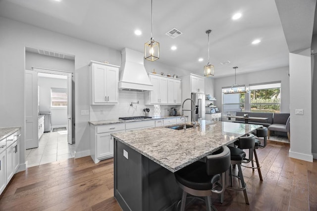 2208 Quarry Loop, Leander, TX 78641 - kitchen featuring custom range hood, hardwood / wood-style flooring, white cabinets, a kitchen island with sink, and recessed lighting