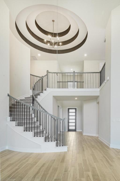 216 Ranchland Pass, Liberty Hill, TX 78642 - stairway featuring wood finished floors, a tray ceiling, a towering ceiling, recessed lighting, and a chandelier